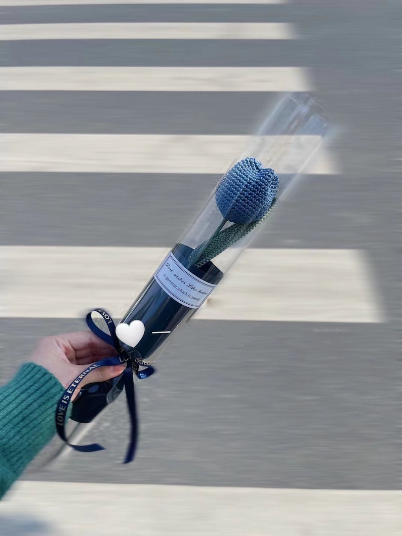 K&ouml;nnte beinhalten: Eine blaue geh&auml;kelte Tulpe in einer transparenten Plastikr&ouml;hre, gebunden mit einem marineblauen Band. Die Blume ist in einer transparenten R&ouml;hre mit marineblauem Boden verpackt. Der Text auf dem Etikett lautet "Mini wishes like heaven in general which is sweet".