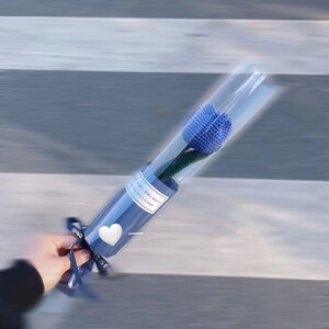 K&ouml;nnte beinhalten: Eine einzelne blaue gestrickte Tulpenblume in einer transparenten Plastikh&uuml;lle, verpackt in blauem Papier mit einem wei&szlig;en Herz und einem Band. Der Text auf dem Papier lautet "...when life seems..."