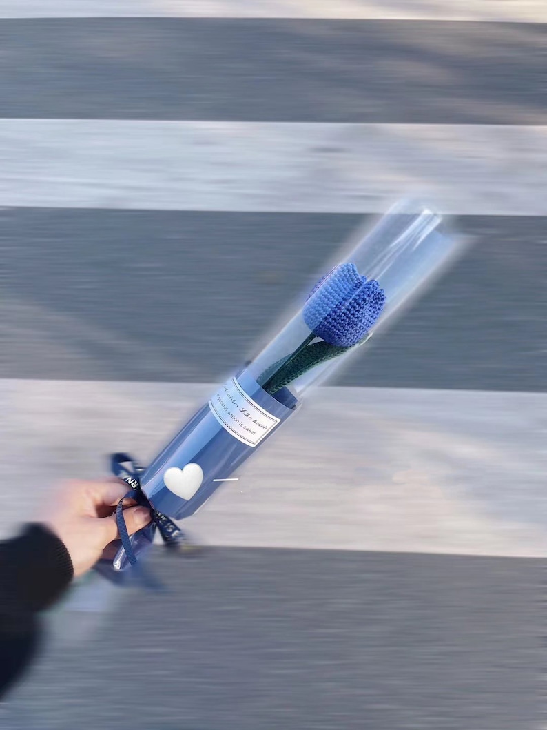 K&ouml;nnte beinhalten: Eine einzelne blaue gestrickte Tulpenblume in einer transparenten Plastikh&uuml;lle, verpackt in blauem Papier mit einem wei&szlig;en Herz und einem Band. Der Text auf dem Papier lautet "...when life seems..."