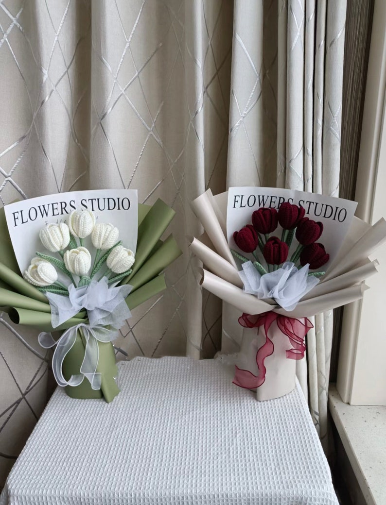 K&ouml;nnte beinhalten: Zwei Str&auml;u&szlig;e geh&auml;kelter Tulpen, einer wei&szlig; und einer rot, in Papier verpackt mit einem Band und dem Text "FLOWERS STUDIO".