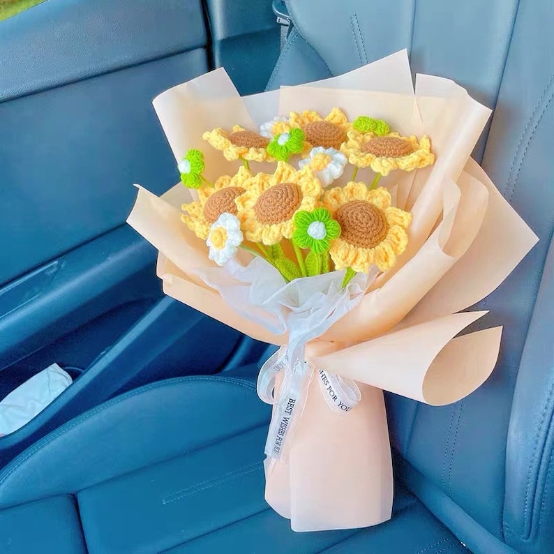 May include: A bouquet of crocheted sunflowers in a peach-colored paper wrapper with a white ribbon tied around it. The ribbon has the text "Best Wishes Ever" and "Here for You" printed on it.