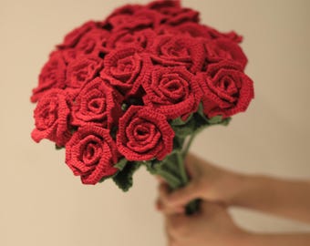 May include: A bouquet of crocheted red roses, held in a person's hands.