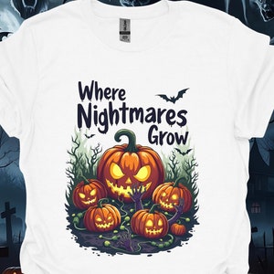 以下が含まれることがあります： ハロウィーンをテーマにしたグラフィックの白いTシャツ。デザインは、光る目と口を持つ大きなオレンジ色のカボチャ、小さなカボチャと「Where Nightmares Grow」というテキストで構成されています。コウモリと不気味な木々がデザインを完成させています。