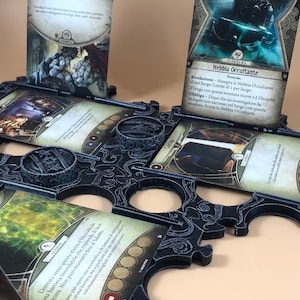 Puede incluir: Un tablero de juego de plástico negro con ranuras para sostener cartas. Las cartas son del juego de mesa Arkham Horror: The Card Game. Las cartas están en italiano. Las cartas son "Sciame di Ratti", "Nebbia Occultante", y "L'entrata verso questa stanza è bloccata da una barriera insondabile che risplende di luce oscura. Non puoi muoverti fino al Salotto."
