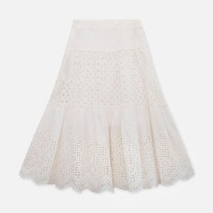 Puede incluir: Una falda blanca de ojal con un diseño escalonado. La falda presenta intrincados patrones calados y un dobladillo festoneado. La falda está hecha de una tela ligera.