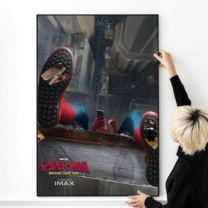 May include: A framed poster featuring the Spider-Man: Brand New Day movie. The image shows Spider-Man in his red and blue suit, holding a phone, with a city backdrop. The poster is being held by a person.