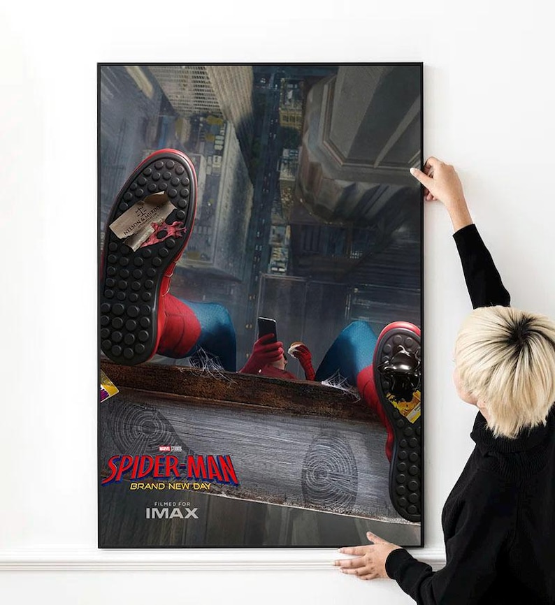 May include: A framed poster featuring the Spider-Man: Brand New Day movie. The image shows Spider-Man in his red and blue suit, holding a phone, with a city backdrop. The poster is being held by a person.