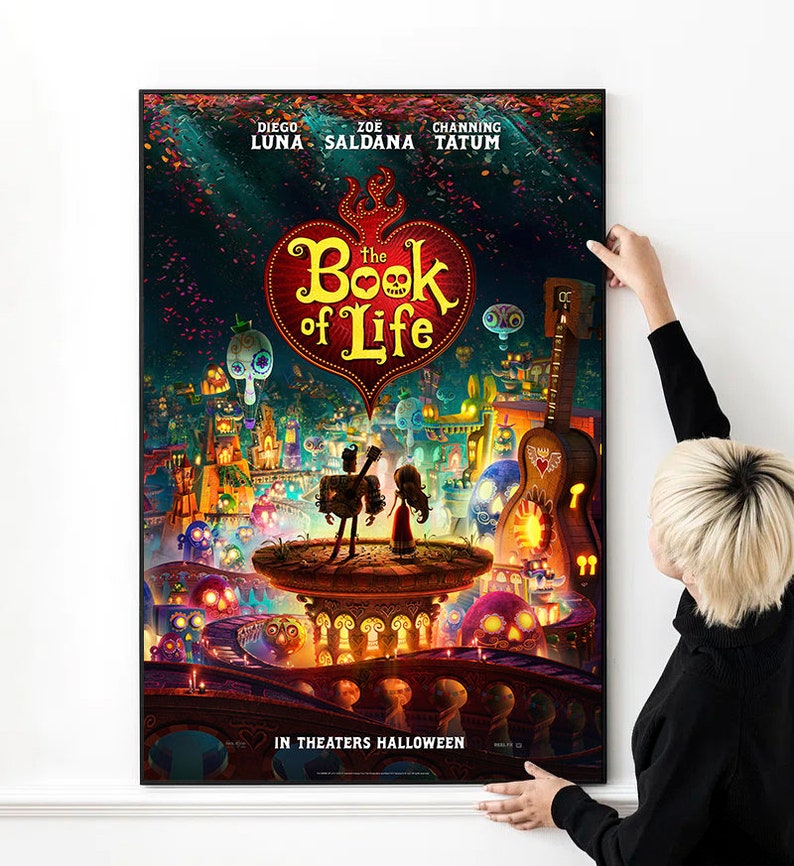 May include: Movie poster for "The Book of Life" featuring Diego Luna, Zoe Saldana, and Channing Tatum. The poster has a red heart with the title "The Book of Life" in white text. The poster is set against a colorful background with a cityscape and skeletons.