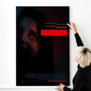 Puede incluir: Un póster de película enmarcado con el título "Obsession" en letras de neón rojas. El póster presenta una imagen oscura del rostro de una persona con un brillo rojo. El texto "Be careful who you wish for" está encima del título.