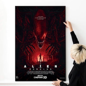 May include: A film poster for the movie "Alien: Romulus" depicting a red alien creature with sharp teeth and claws. The alien is in a threatening pose, with its claws extended. The poster also features a human character standing in the background, looking up at the alien. The text "Alien: Romulus" is displayed in large, bold letters at the bottom of the poster.
