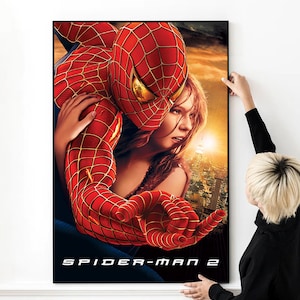 May include: A movie poster for Spider-Man 2 featuring Spider-Man in his red and blue suit holding a woman in a white tank top. The poster has a cityscape background with a sunset in the distance. The text "SPIDER-MAN 2" is at the bottom of the poster.