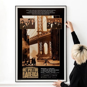 May include: A vintage movie poster for the film "Once Upon a Time in America" featuring a black and white image of the Brooklyn Bridge and a group of men walking in the street. The poster has a gold and black color scheme and includes the film's title and credits.