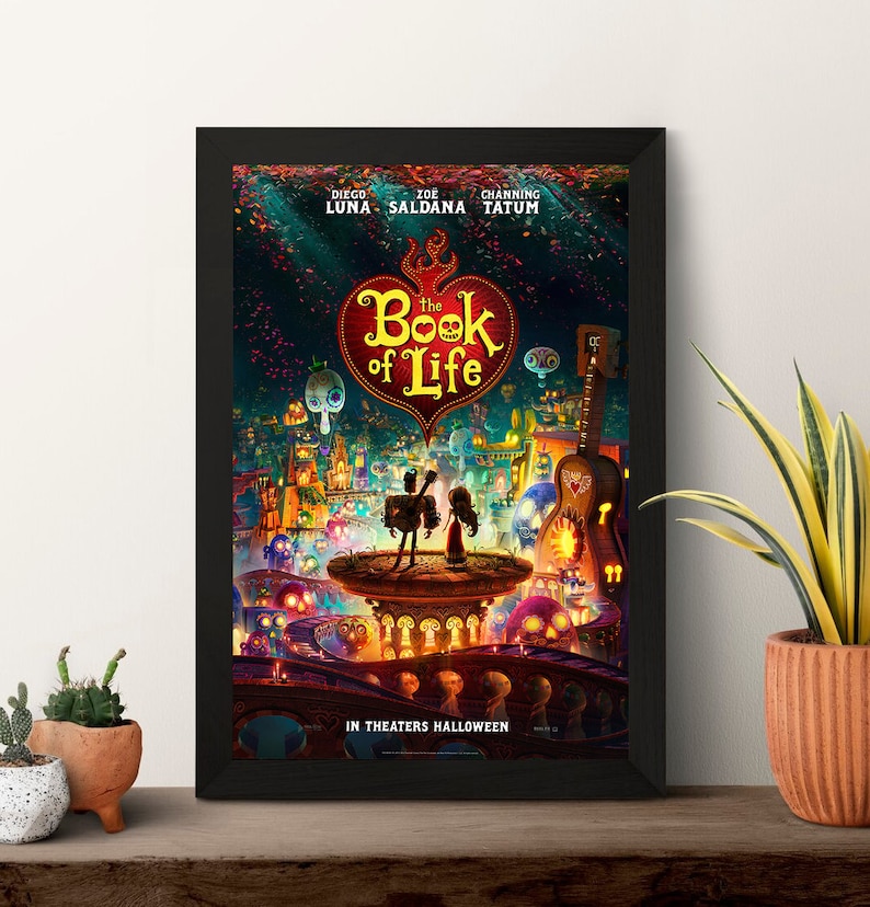 May include: A movie poster for the animated film "The Book of Life" featuring a red heart with the title in white text. The poster features a colorful illustration of a town with a couple standing on a platform. The poster includes the names of the actors Diego Luna, Zoe Saldana, and Channing Tatum.