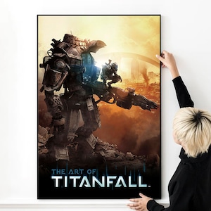 Könnte beinhalten: Ein gerahmtes Poster mit einem großen Mech und einer kleineren Figur vor dem Hintergrund einer brennenden Stadt. Der Titel des Posters lautet "THE ART OF TITANFALL" in Weiß und Blau, mit einem schwarzen Rahmen.