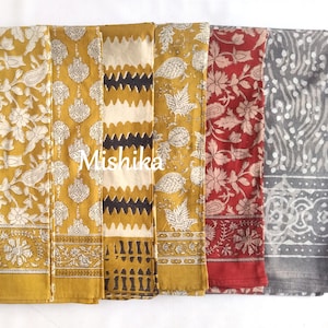 Könnte beinhalten: Eine Sammlung von sechs gefalteten rechteckigen Stoffstücken mit verschiedenen Blockdruckmustern in Senfgelb, Dunkelrot und Grau. Die Designs umfassen florale Motive, Paisleymuster und geometrische Streifen. Das Wort Mishika ist in Weiß aufgedruckt.