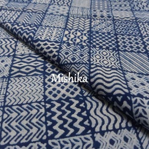 Puede incluir: Una tela de color azul oscuro y blanco con un patrón de cuadrícula repetitivo de varias formas geométricas, incluyendo líneas onduladas, chevrones y diamantes. La palabra Mishika está impresa en blanco en el centro del tejido doblado.
