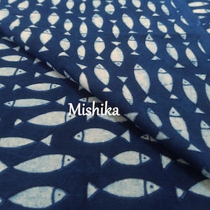 May include: Dark blue fabric with a repeating pattern of white fish. The fabric is folded, showing the texture and depth of the material. The word "Mishika" is printed on the fabric.
