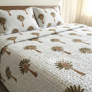 Puede incluir: Juego de cama acolchado blanco con un patrón repetido de palmeras marrones. El juego incluye un edredón y dos fundas de almohada. Las costuras crean un efecto texturizado. La ropa de cama está sobre una estructura de cama de madera.