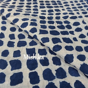 May include: White fabric with a blue and white geometric pattern. The pattern is made up of small, irregular shapes that resemble dots. The fabric is folded in half, and the word "Mishika" is printed on the fabric.