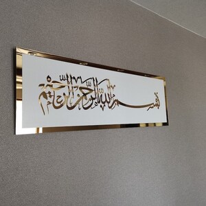 Op de afbeelding: Een gouden lijst met een witte achtergrond met Arabische kalligrafie in goud. De tekst luidt "Bismillah Al-Rahman Al-Rahim", wat vertaald wordt als "In de naam van Allah, de Meest Barmhartige, de Meest Genadevolle."