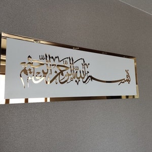 Op de afbeelding: Een gouden lijst met een witte achtergrond met gouden Arabische kalligrafie. De kalligrafie luidt "Allah" en "Muhammad".