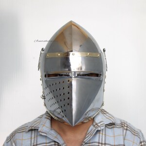 May include: A silver helmet with a pointed top and a brass trim. The helmet has a face mask with a series of small holes for ventilation.