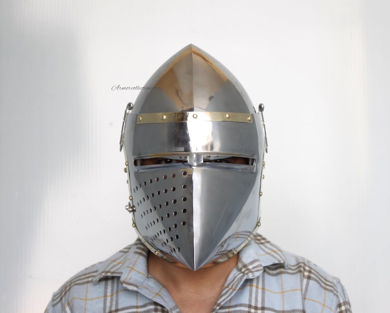 May include: A silver helmet with a pointed top and a brass trim. The helmet has a face mask with a series of small holes for ventilation.