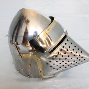 May include: A silver helmet with a pointed visor and a brass trim. The visor is perforated with small holes.