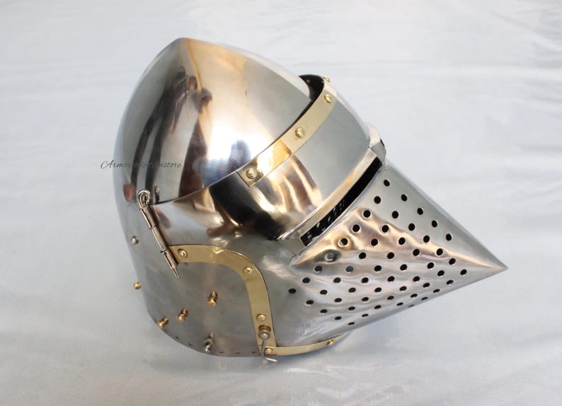 May include: A silver helmet with a pointed visor and a brass trim. The visor is perforated with small holes.