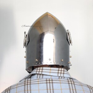 May include: A silver helmet with a pointed top and a visor. The helmet has a series of rivets around the edge and two metal pieces on the sides.