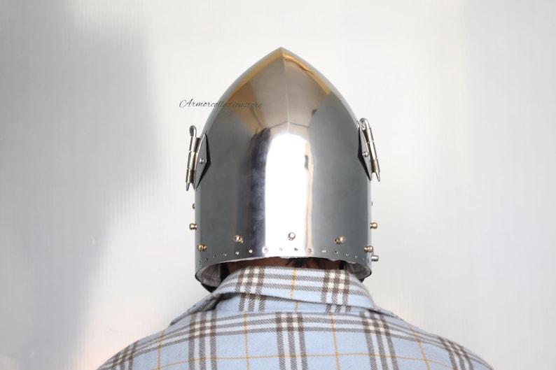 May include: A silver helmet with a pointed top and a visor. The helmet has a series of rivets around the edge and two metal pieces on the sides.
