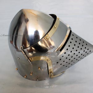 May include: A silver helmet with a brass visor and a pointed, perforated nasal. The helmet has a hinged visor and a strap on the back.