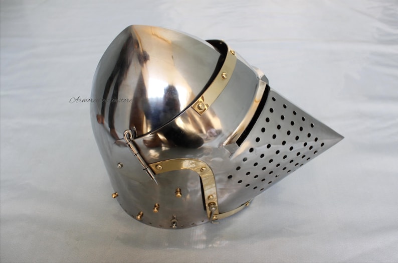 May include: A silver helmet with a brass visor and a pointed, perforated nasal. The helmet has a hinged visor and a strap on the back.