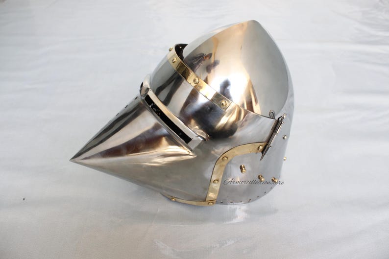 May include: A silver helmet with a pointed visor and brass accents. The helmet has a hinged visor and a brass strap on the side.