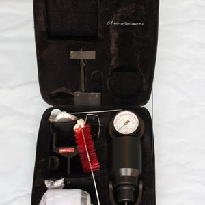 Puede incluir: Una maleta de transporte negra con un medidor de humedad negro, un cepillo rojo, un recipiente de plástico blanco y una herramienta negra con una etiqueta blanca que dice "BAL-4gm."