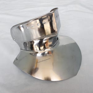 Könnte beinhalten: Ein poliertes, silberfarbenes Gorget, ein Teil mittelalterlicher Rüstung, zum Schutz von Hals und oberer Brust. Das Metall reflektiert das Licht und hebt seine geschwungene Form und die Nietdetails hervor. Das Gorget liegt auf einer weißen Oberfläche.
