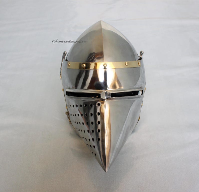 May include: A silver helmet with a pointed visor and a brass band around the top. The helmet has a small, pointed nose guard and a series of small holes in the visor.