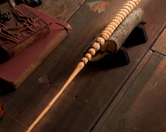 May include: A wooden wand with a unique design featuring a series of carved spheres. The wand is resting on a wooden stand.
