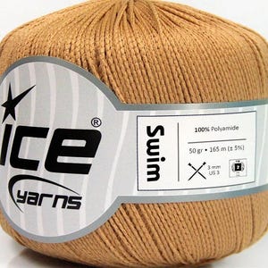 May include: A ball of tan yarn with a paper label reading Ice Yarns Swim, 100% Polyamide, 50 gr, 165 m, and 3 mm US 3. The yarn is a solid light brown colour with a smooth, twisted texture, wrapped in a white band with black text and graphics.
