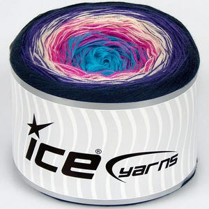 May include: A cylindrical cake of yarn featuring a gradient color transition from a deep navy blue outer edge to a bright turquoise center, passing through shades of cream and magenta. A white paper label wraps around the base with the text ice yarns.