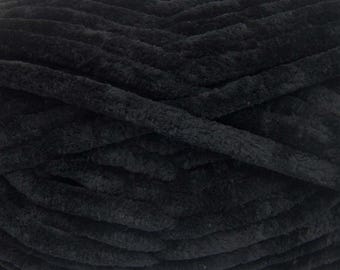 Könnte beinhalten: Ein Knäuel aus einfarbig schwarzem Garn mit einer dicken, plüschigen und samtigen Textur. Das Garn ist in einem dichten, geschichteten Muster gewickelt und zeigt die weichen, flauschigen Fasern sowie die tiefe, gleichmäßige schwarze Farbe.