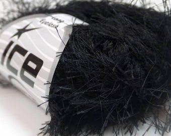 May include: A skein of black eyelash yarn with a textured, fuzzy appearance. The yarn is wrapped in a white paper label featuring the brand name Ice and the text Eyelash printed in black. The fibers are thin, long, and create a dense, dark volume.