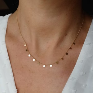 Peut inclure: Un collier en or avec de petits pendentifs ronds. Le collier est porté par une personne.