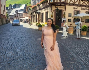May include: A woman in a peach-colored tulle dress stands in a cobblestone street in front of a building with a sign that reads "Hotel Alt" and "Reception".