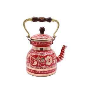 Puede incluir: Una tetera de cobre rojo con un asa dorada y diseños florales intrincados. La tetera tiene una tapa con un pequeño pomo en la parte superior.