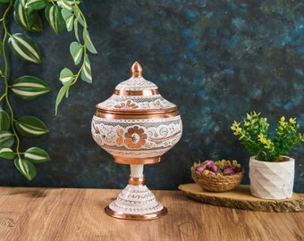 Peut inclure: Bol décoratif en sucre blanc et cuivre avec des motifs floraux complexes. Le bol a un couvercle et repose sur un piédestal.