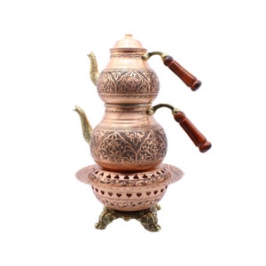 May include: A traditional Turkish copper tea set with intricate engraved designs. The set includes two teapots with wooden handles and a stand with a decorative base.