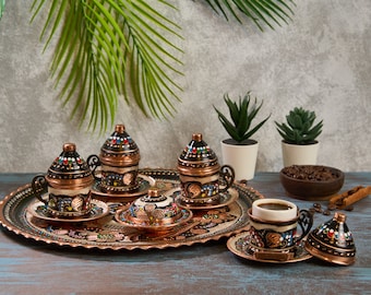 May include: A set of six Turkish coffee cups and saucers with intricate hand-painted designs in black, white, and red. The cups and saucers are made of copper and have a traditional Turkish design. The set is displayed on a copper tray with a decorative border.