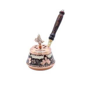 May include: A copper incense burner with a decorative floral design and a wooden handle. The burner has a small bird-shaped finial on top.