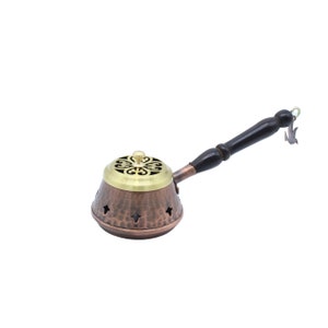 May include: A copper and brass incense burner with a wooden handle. The burner has a decorative lid with a floral design and a hammered finish.